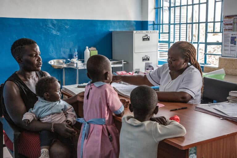 Rosalyn sits at the clinic with her three children to receive a check-up from the nurse.